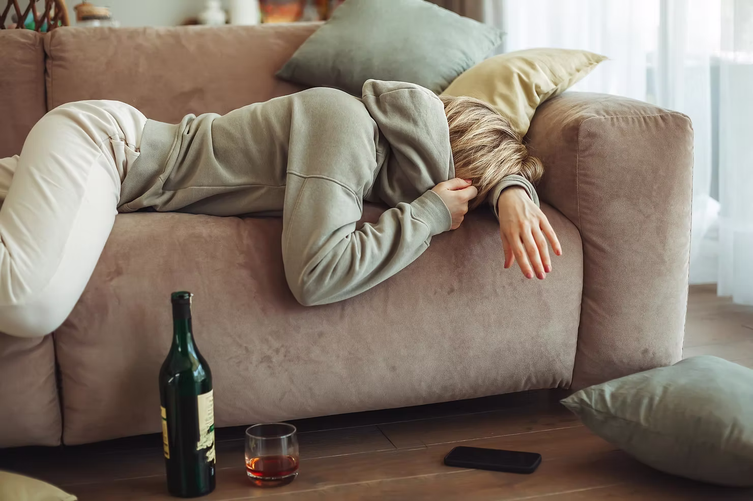 Kobieta leżąca na kanapie z bólem głowy obok butelki alkoholu - objawy kaca i złe samopoczucie po alkoholu
