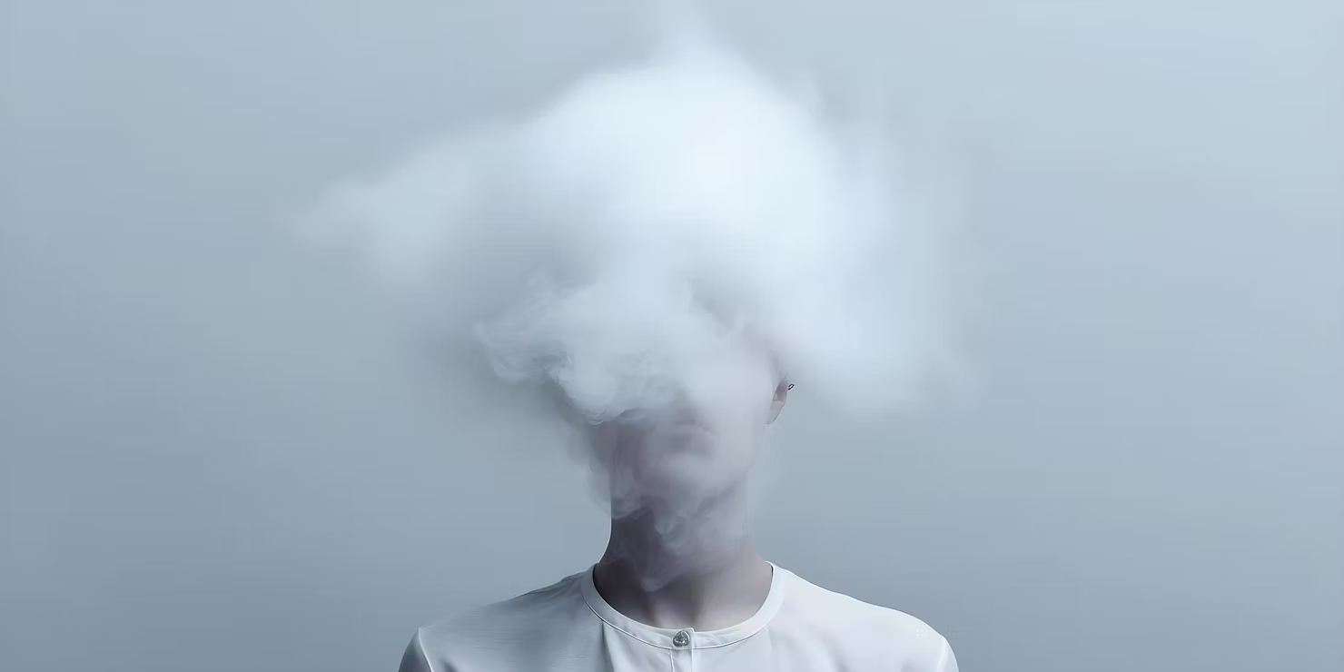 Osoba z głową ukrytą w chmurze białej mgły - wizualna metafora mgły mózgowej (brain fog) i problemów z koncentracją
